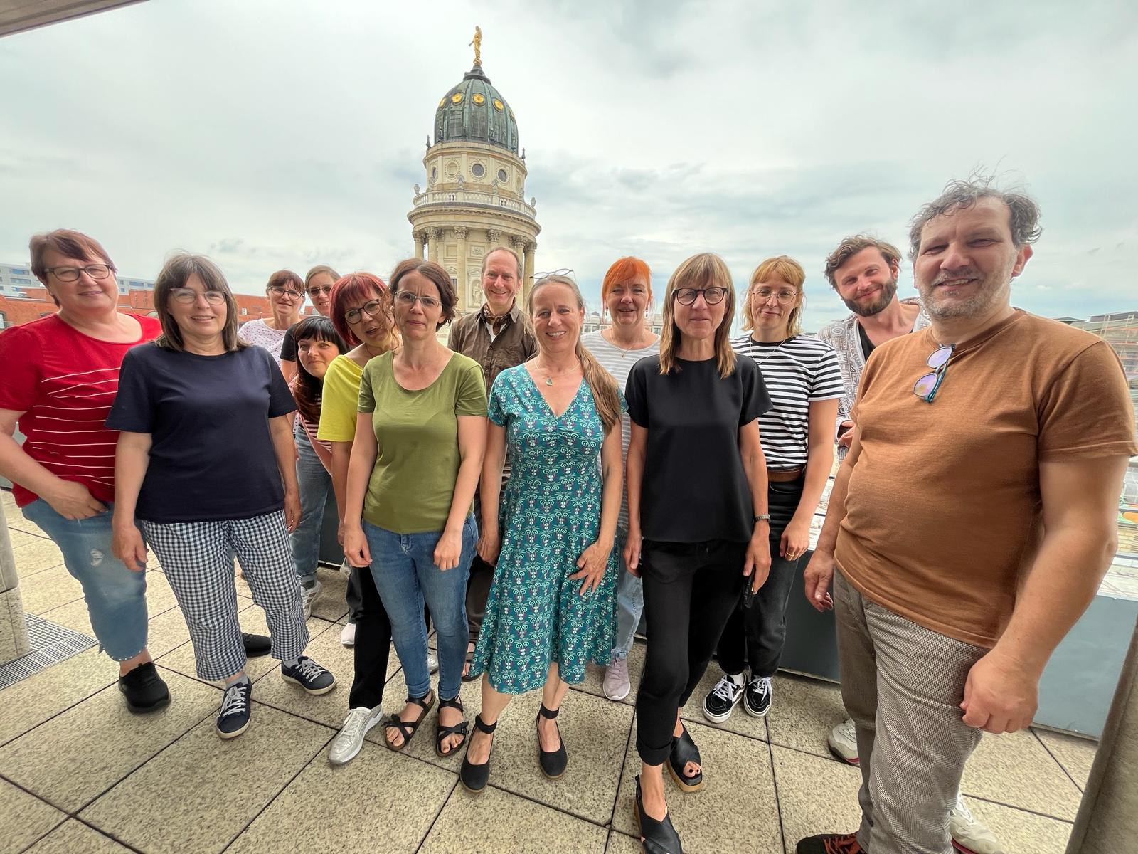 Mitglieder der Lagfa Brandenburg auf einem Balkon am Gendarmenmarkt Berlin lächeln in die Kamera.